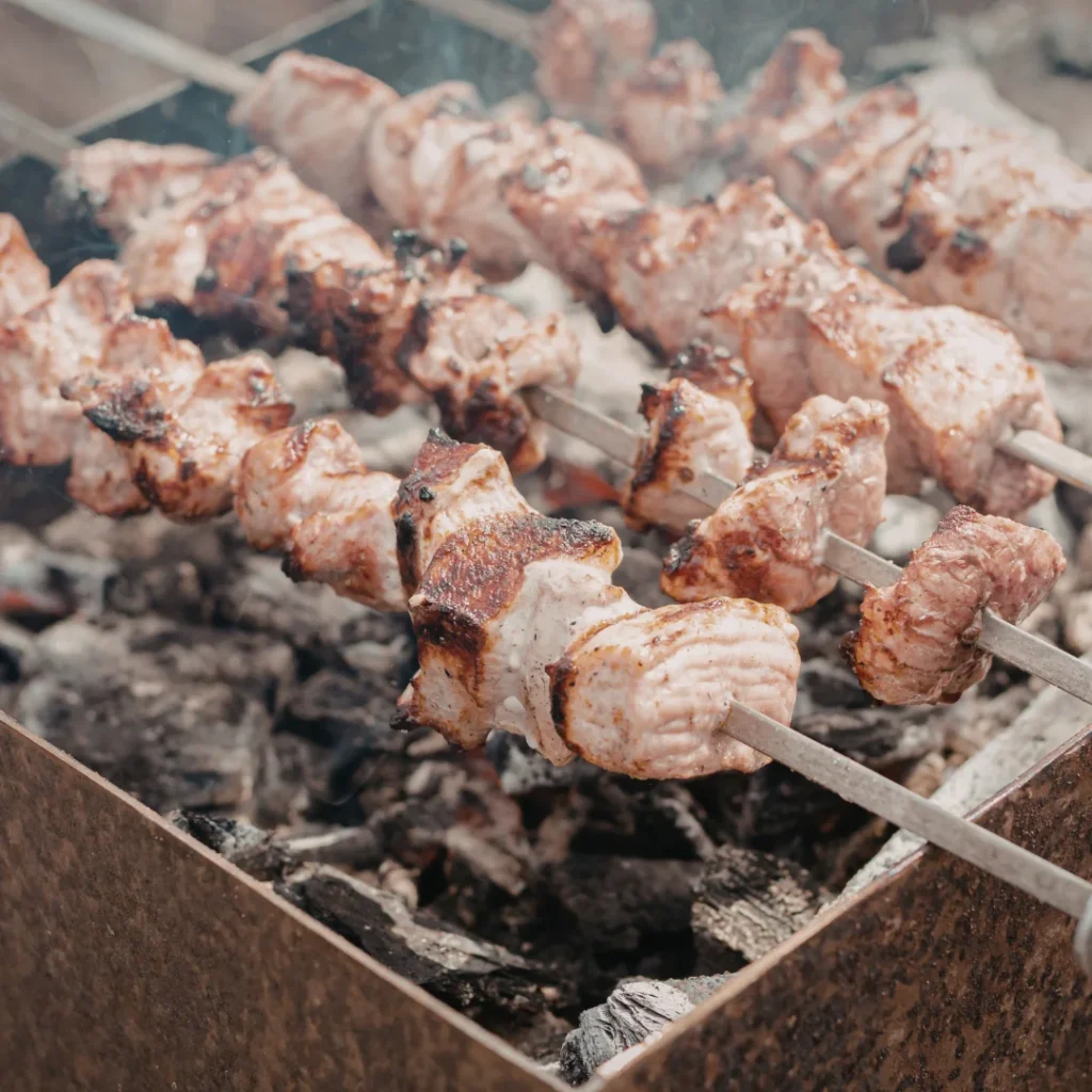 Churrasqueira com peças de carne assando no espeto sobre brasa