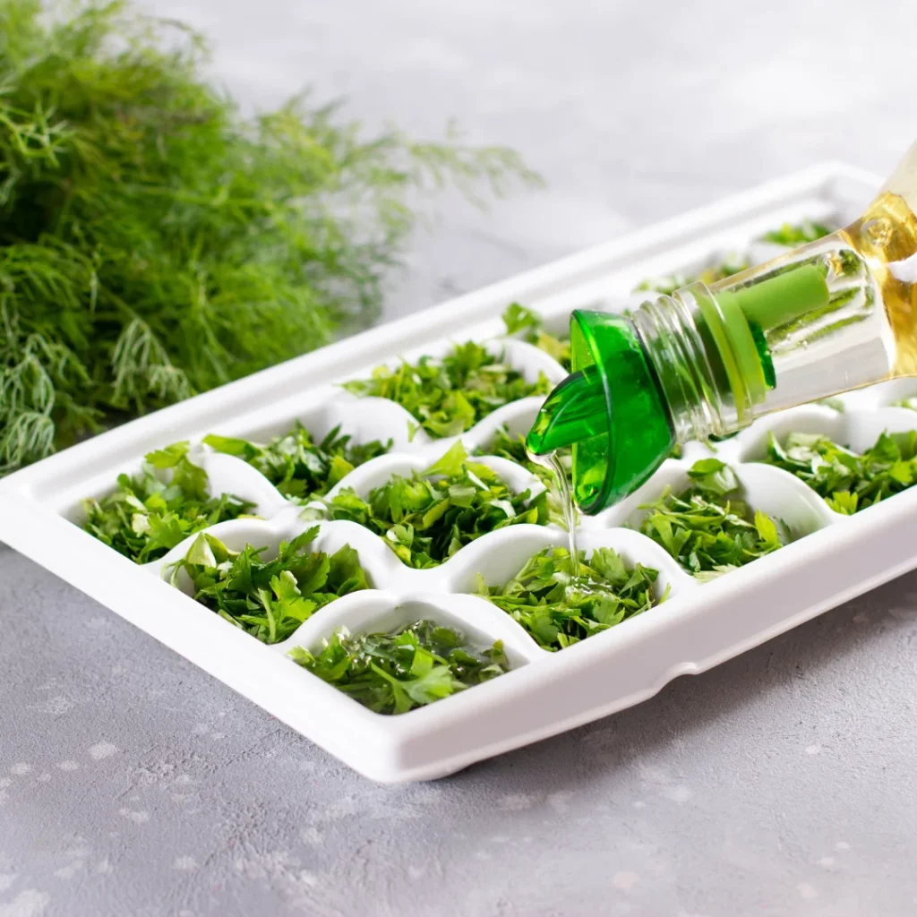 Forma de gelo com cubos contendo ervas picadas e azeite verde, prontos para congelar